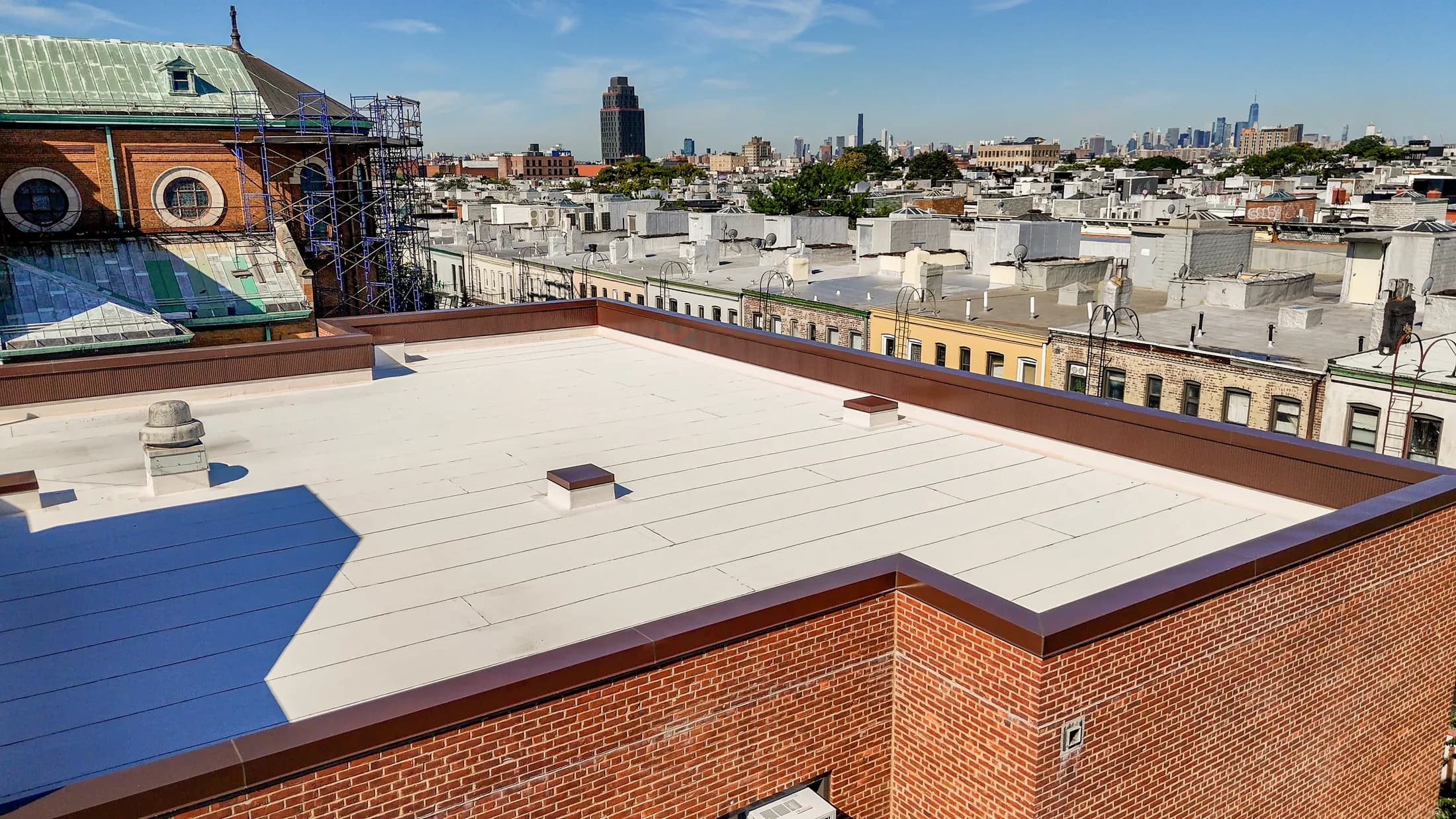 Completed light-colored roof membrane at St. Matthias RC Church with Ridgewood visible beyond